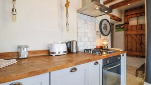 Una cocina con encimera de madera, estufa a gas, cafetera, hervidor y lámpara colgante.