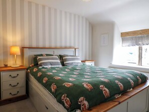 A bedroom with a bed, a bedside table with a lamp, a dresser with drawers, and a window with a view. - 2 Knoll Mount (Matlock)