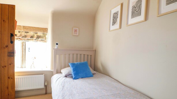 Un dormitorio con cama, ventana, radiador y cuadros en la pared.