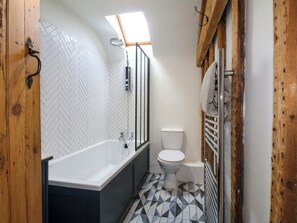 A bathroom with a herringbone tile pattern, a white bathtub, a toilet, and a wooden door. - 2 Knoll Mount (Matlock)