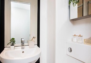 A bathroom with a white sink, a mirror, a potted plant, and a small cabinet with toiletries. - Student Only En-suite at Stapleton House near London Metropolitan University (London)