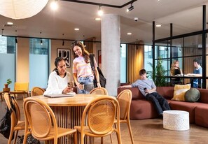 A modern interior with a round wooden table, wicker chairs, a red sofa, and a white coffee table. - Student Only En-suite at Stapleton House near London Metropolitan University (London)