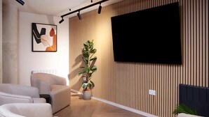 Ein modernes Wohnzimmer mit einem flachbildfernseher an der Wand, einer Topfpflanze und einem Sofa.