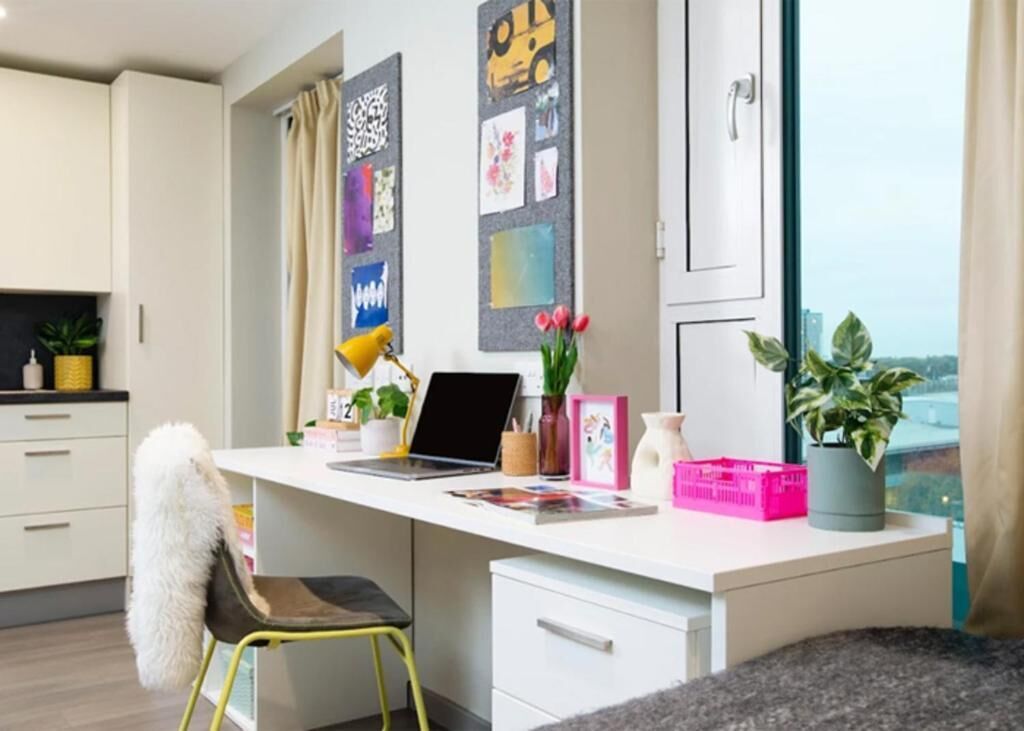 A modern office space with a desk, chair, laptop, potted plants, and artwork on the wall.