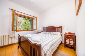 Une chambre à coucher avec un lit en bois, une table de chevet, une fenêtre donnant sur un paysage verdoyant et un radiateur.