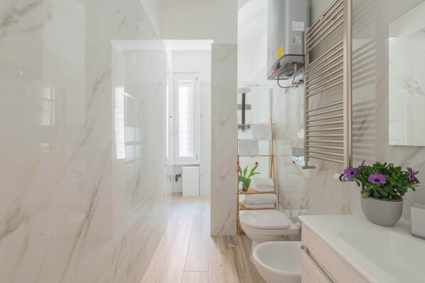 Een moderne badkamer met een marmeren vloer, een toilet, een wastafel en een douchehoek.