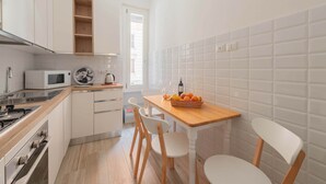 A compact kitchen with white cabinets, a microwave, a stove, and a wooden table with chairs. - Marmorata 169 - Loft in Testaccio (Rome)
