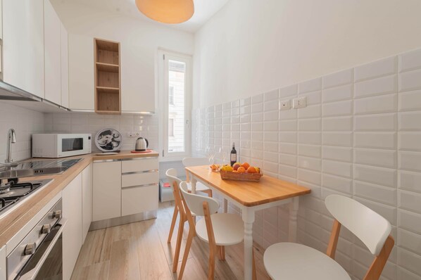 A compact kitchen with white cabinets, a microwave, a stove, and a wooden table with chairs. - Marmorata 169 - Loft in Testaccio (Rome)