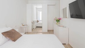 A modern bedroom with a bed, bedside table, and a dresser. There is a mirror on the wall and a door leading to another room. - Marmorata 169 - Loft in Testaccio (Rome)