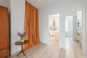 A room with a wooden floor, a table with a vase of flowers, a curtain, and an open doorway leading to a kitchen area. - Marmorata 169 - Loft in Testaccio (Rome)