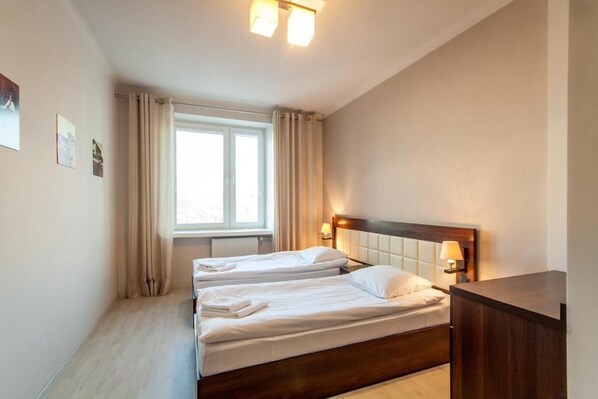 A hotel room with two beds, a window with curtains, a bedside table with a lamp, and a wooden headboard. - Avion Hotel (Świdnik)