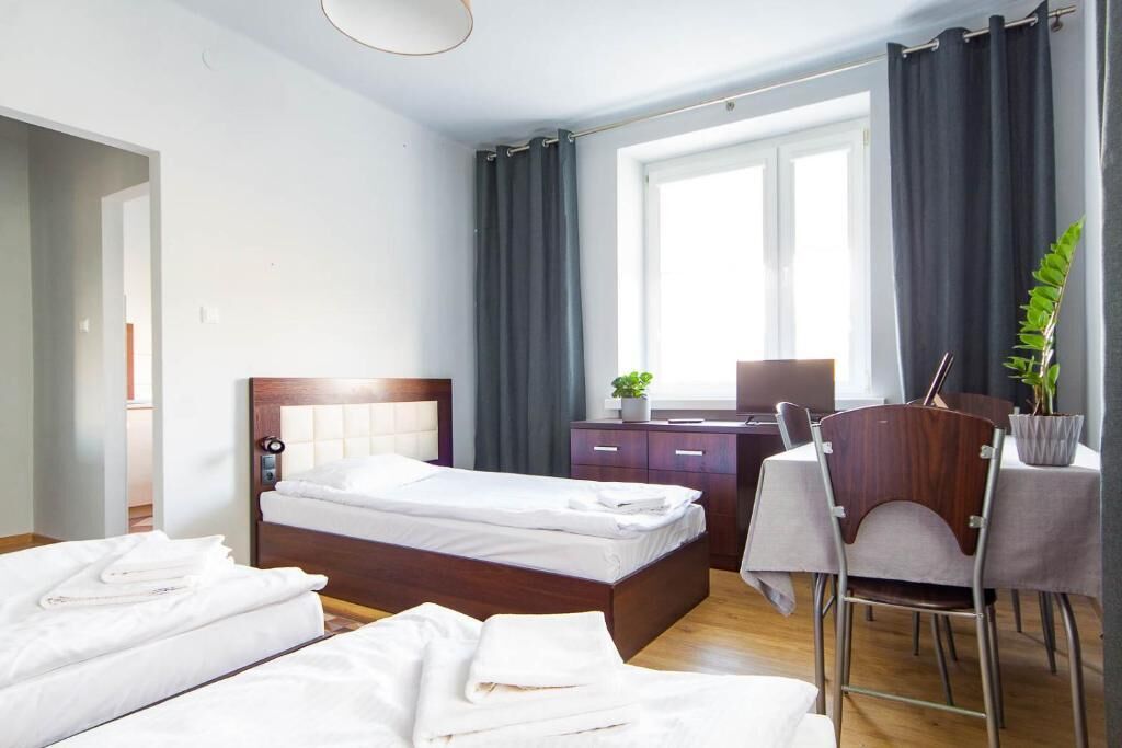 Habitación de hotel con dos camas, un escritorio, una silla, una ventana con cortinas y una planta.