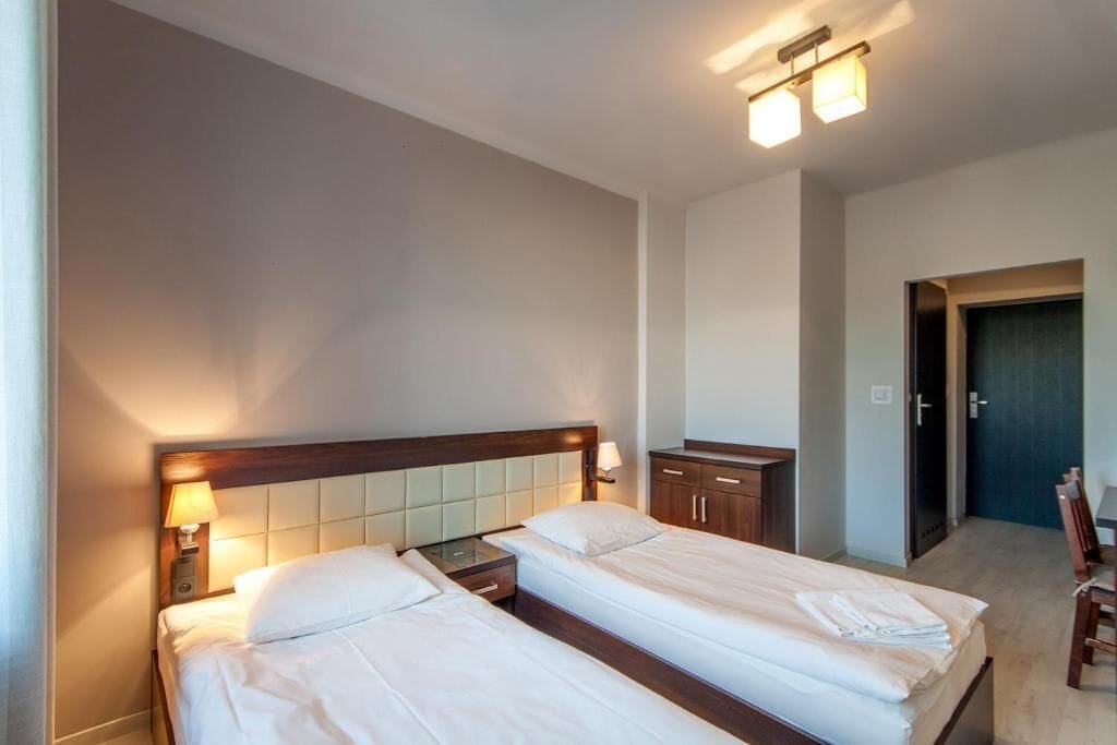 A hotel room with two beds, a nightstand, a dresser, and a door leading to another room.