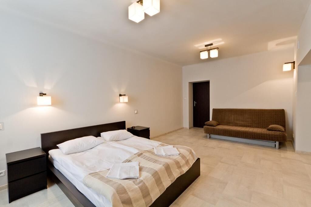 Un dormitori amb llit, taules de nit, un sofà i llums penjades a la paret.