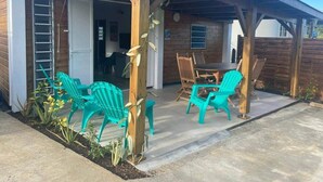 Een overdekt terras met buitenmeubilair, een houten constructie en een deur naar een binnenruimte.