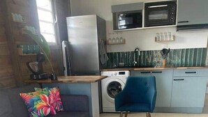 Een gezellig, compact ingerichte ruimte met een bank, een houten bijzettafeltje, een wasmachine en een magnetron.