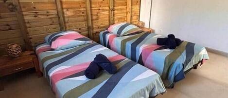 A room with two beds, wooden walls, an air conditioning unit, and a tiled floor.