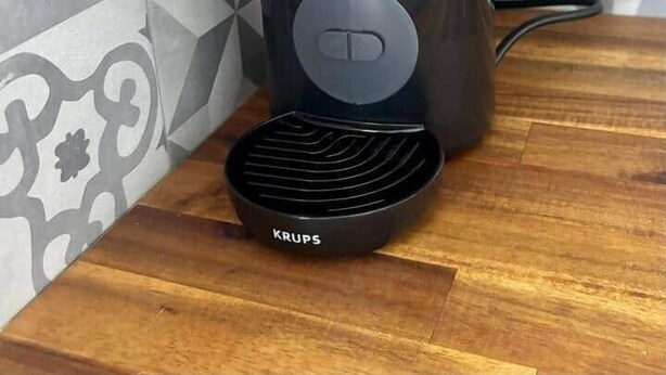 Eine Krups-Kaffeemaschine auf einer Holz Arbeitsplatte mit einem gemusterten Spritzschutz.