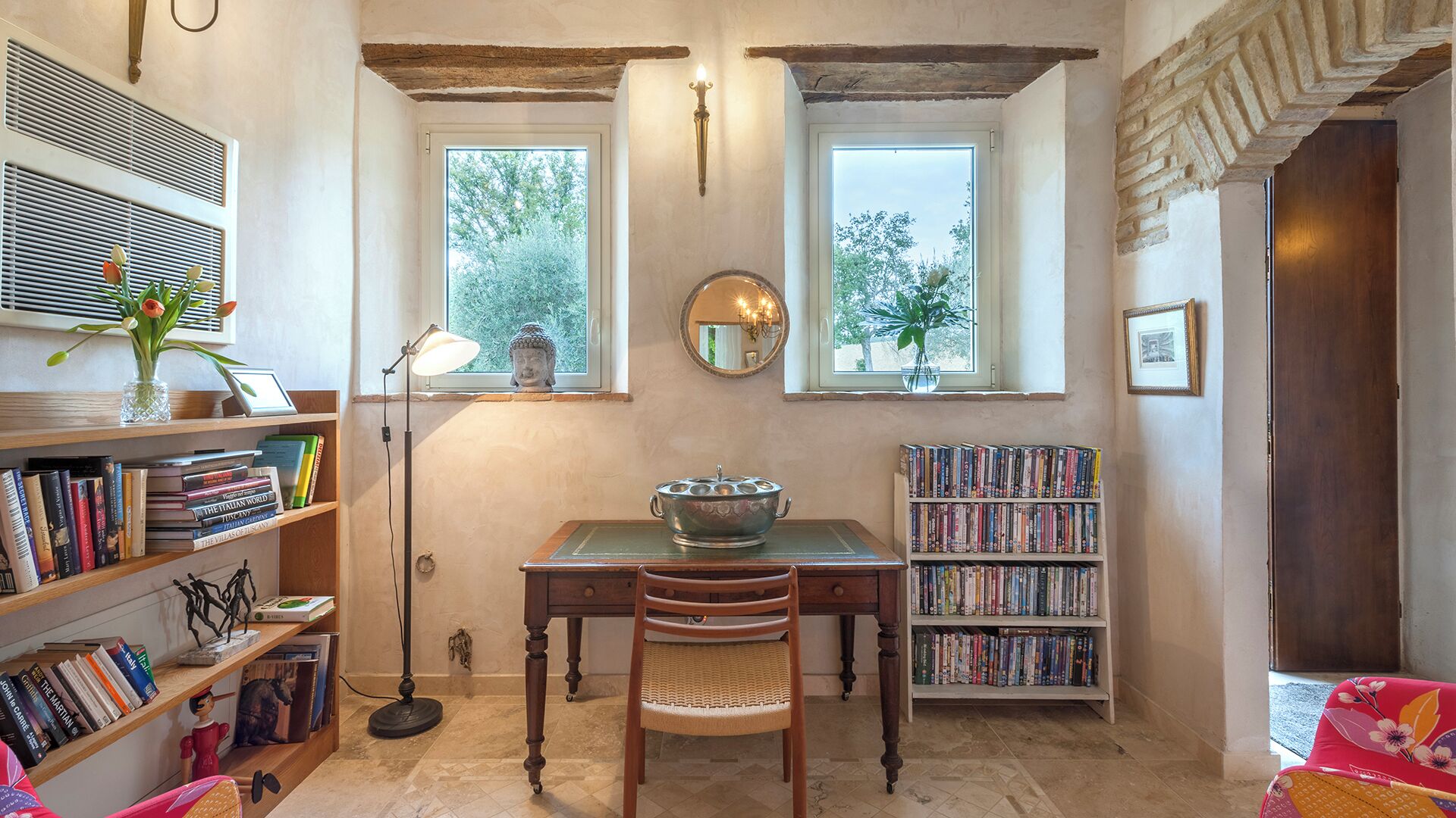 Une pièce avec une grande fenêtre, une statue de Bouddha, une bibliothèque, une table avec un bol et une chaise.