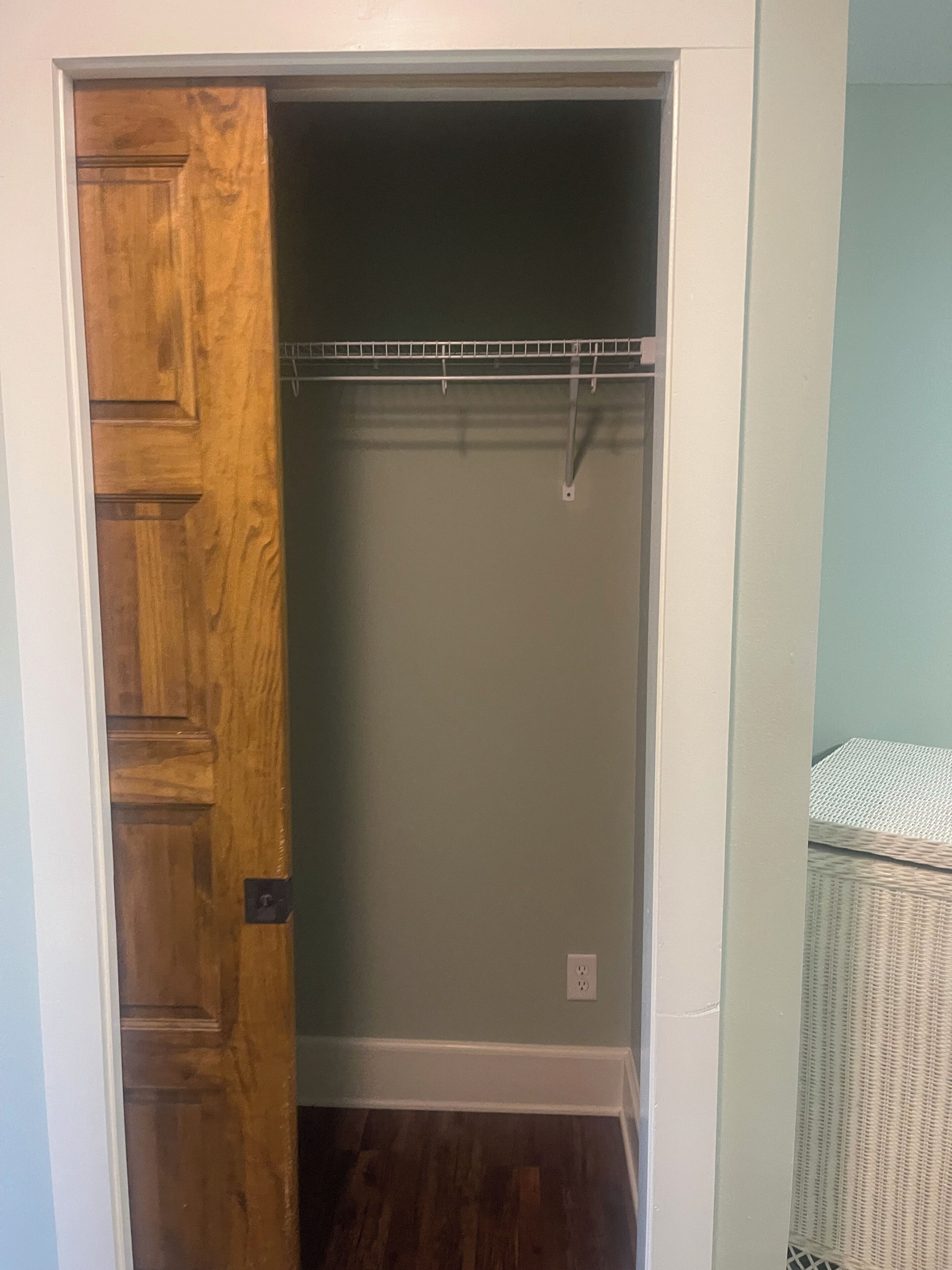 Un armadio con porta in legno, un'asta metallica e un cesto di vimini bianco.