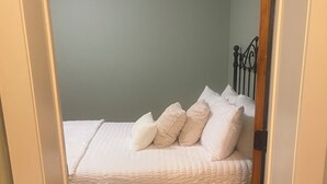 A bedroom with a bed, pillows, a wooden headboard, and a wooden floor.