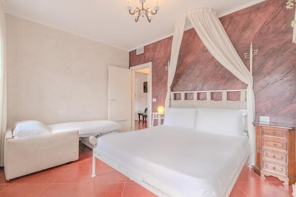 A bedroom with a large bed, a smaller sofa, a nightstand, and a mirror. - Suites Train Station Mestre (Mestre)