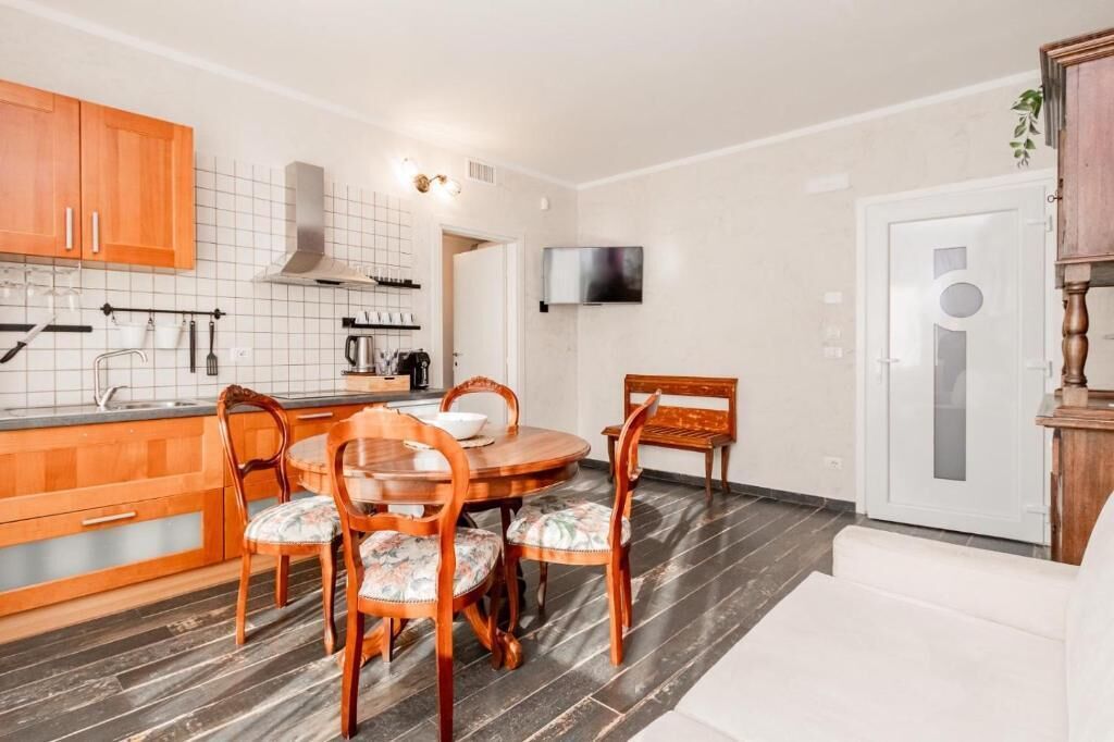 A compact kitchen with wooden cabinets, a dining table with chairs, and a TV mounted on the wall.