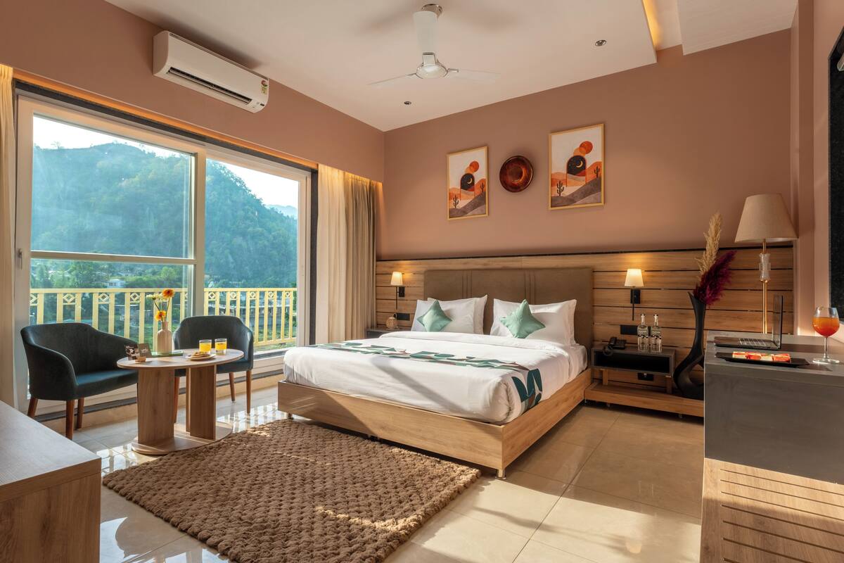 A hotel room with a bed, bedside table, lamp, and a view of the outdoors.
