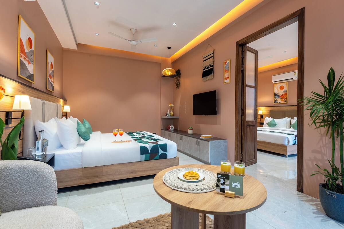 A modern hotel room with a bed, bedside table, lamp, and a dining area with a table set for breakfast.