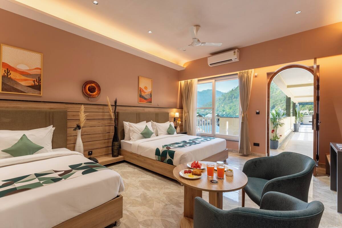 A hotel room with two beds, a dining table with breakfast, a balcony, and a view of greenery.
