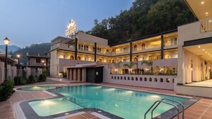 Ein Hotel mit Schwimmbad, mehreren Balkonen und einer Bergkulisse.