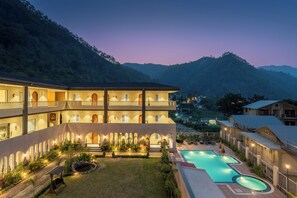 Ein mehrstöckiges Hotel mit Schwimmbad, Außenbereich zum Sitzen und einer Bergkulisse.