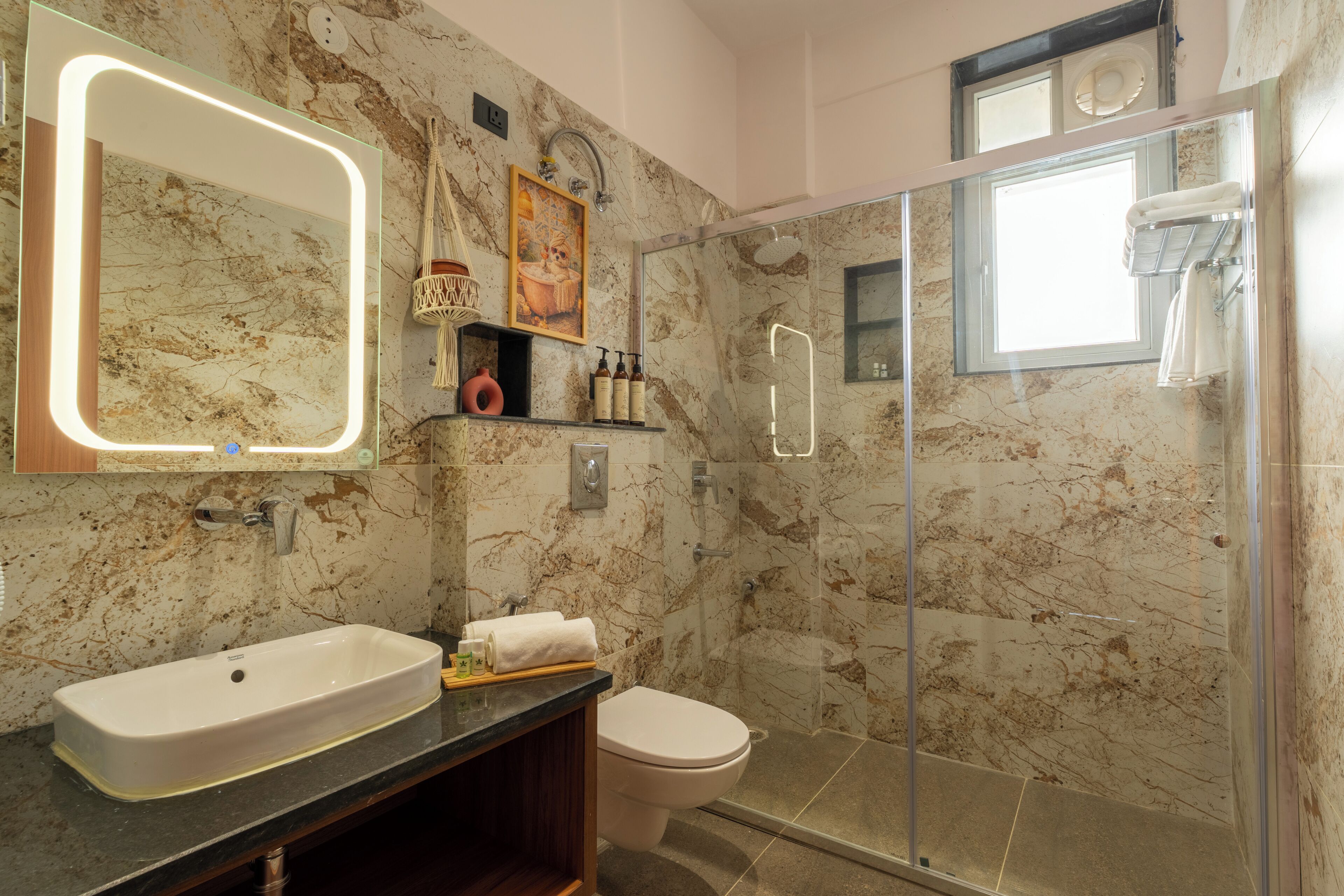 Une salle de bain avec un lavabo en marbre, des toilettes, une douche en verre et un grand miroir avec éclairage.