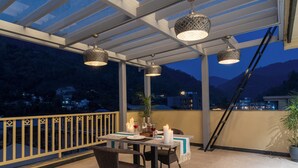An outdoor dining area with a table set for two, a potted plant, and a view of the mountains.