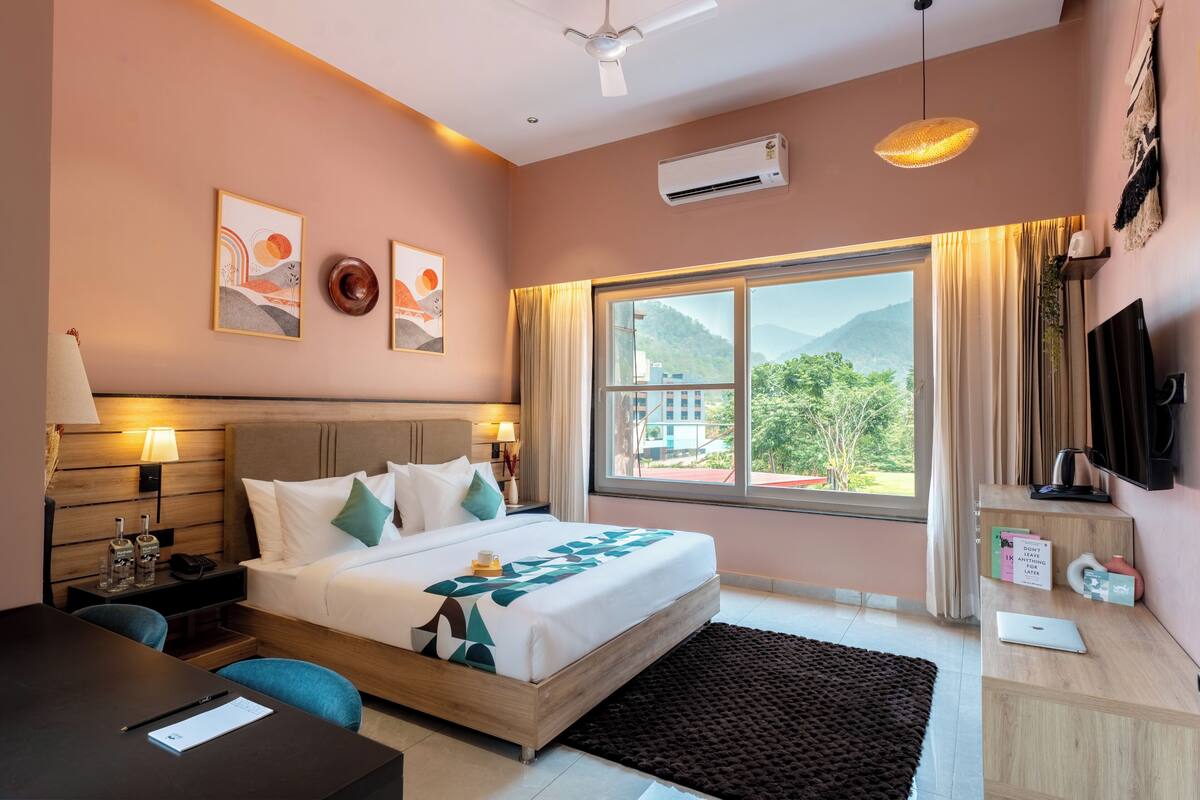 A hotel room with a bed, desk, and window with a mountain view.