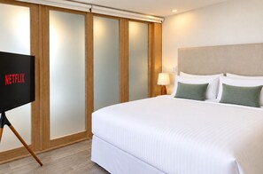 A hotel room with a bed, a TV on a stand, a nightstand with a lamp, and a sliding door with frosted glass panels. - Unique house with direct access to the beach, four bedrooms, balcony and design (Ciudad de Panamá)