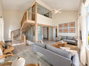 A spacious living area with a high ceiling, a staircase leading to an upper level, a grey sofa set, and a ceiling fan. - Unique house with direct access to the beach, four bedrooms, balcony and design (Ciudad de Panamá)
