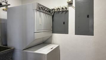 A laundry room with a front-loading washer and dryer, a control panel with multiple dials, and a wall-mounted electrical panel.