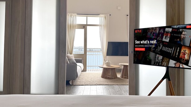 Ett hotellrum med en balkong, en säng, en TV och utsikt över havet.