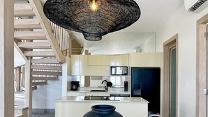 Ett modernt kök med en central köksö, en hängande lampa och en trappa som leder upp till en övre våning.