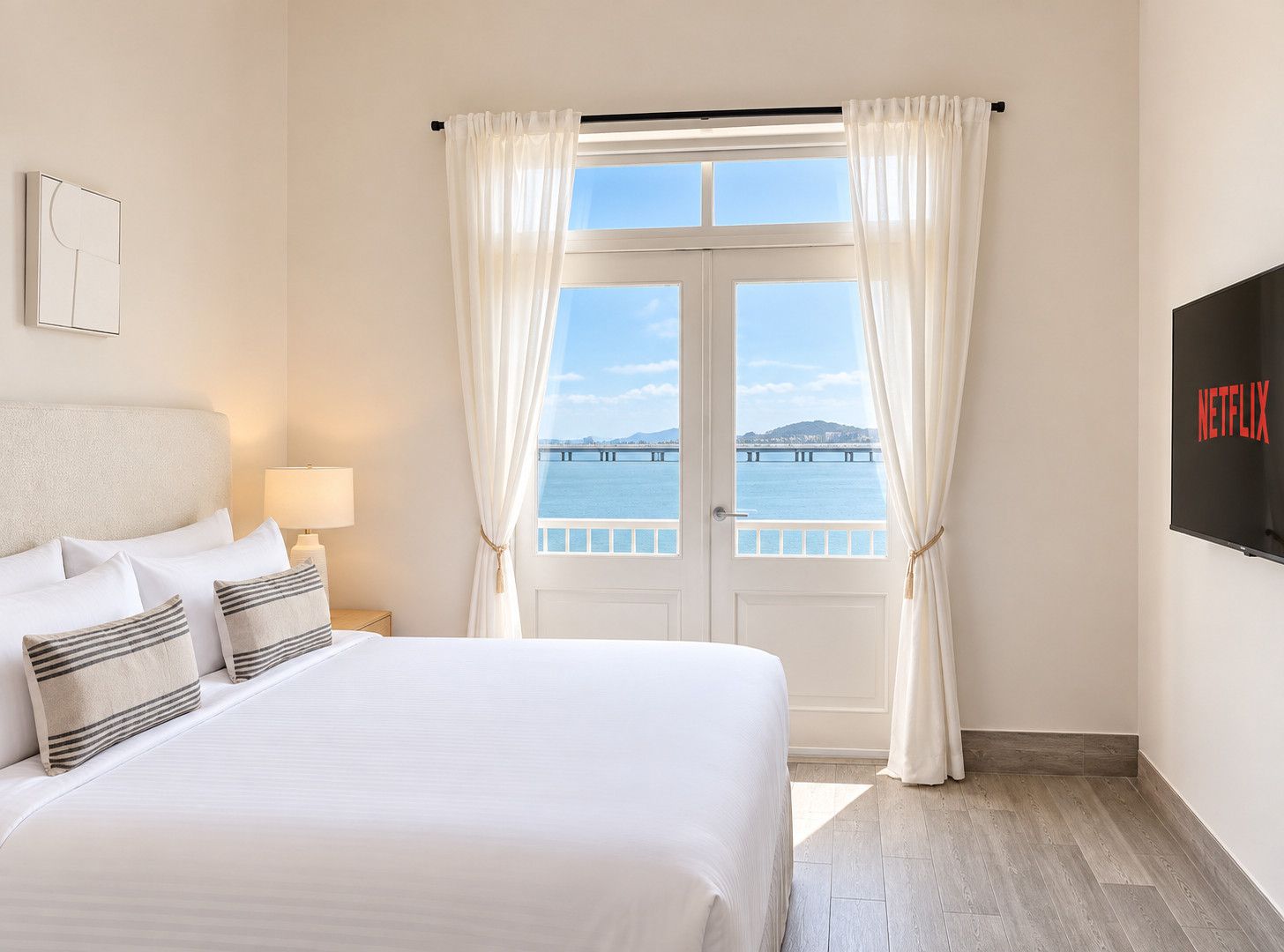Een hotelkamer met een bed, een televisie, een raam met gordijnen en uitzicht op een brug.