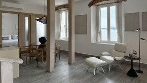 Ett modernt hotellrum med en matplats, ett stort fönster med gardiner, en soffa och ett litet bord med en lampa.