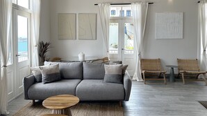 Ett modernt vardagsrum med en grå hörnsoffa, två sidobord, utsikt över naturen och ett stort fönster med gardiner.