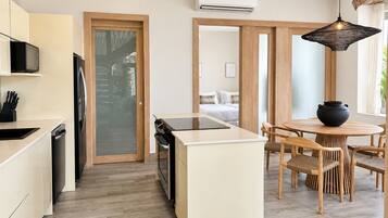 Una cocina moderna con una isla central, una zona de comedor con una mesa redonda y sillas, y un dormitorio visible al fondo.