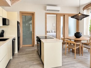 A modern kitchen with a central island, a dining area with a round table and chairs, and a visible bedroom in the background. - Unique house with direct access to the beach, four bedrooms, balcony and design (Ciudad de Panamá)