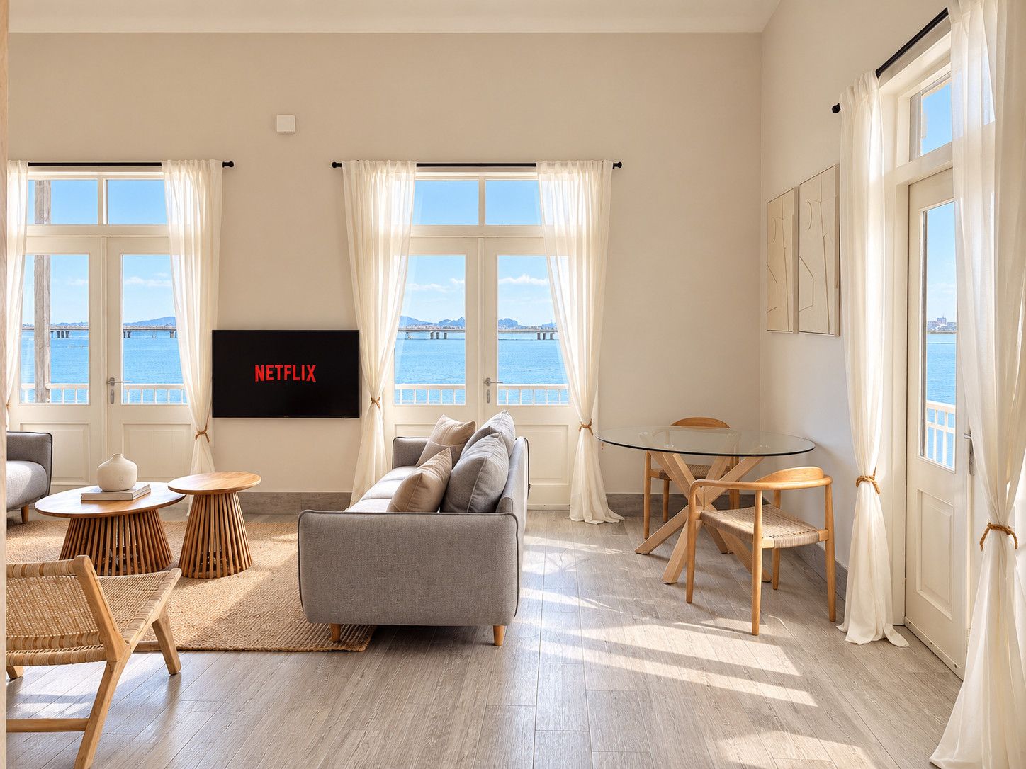 Una sala moderna con un sofá gris, mesas auxiliares de madera, una mesa de centro de vidrio y un televisor de pantalla plana montado en la pared.