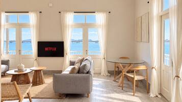 Una sala moderna con un sofá gris, mesas auxiliares de madera, una mesa de centro de vidrio y un televisor de pantalla plana montado en la pared.