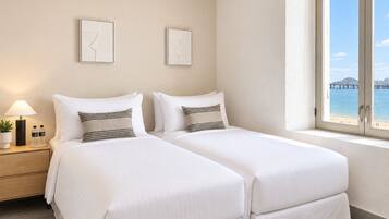 A hotel room with two beds, a nightstand with a lamp and water bottles, and a window with a view of a bridge and water.