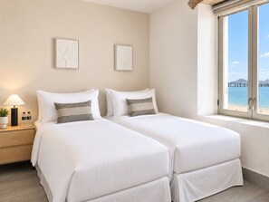 A hotel room with two beds, a nightstand with a lamp and water bottles, and a window with a view of a bridge and water.