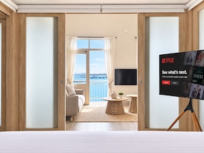 A hotel room with a balcony, a bed, a TV on a stand, and a view of the sea.